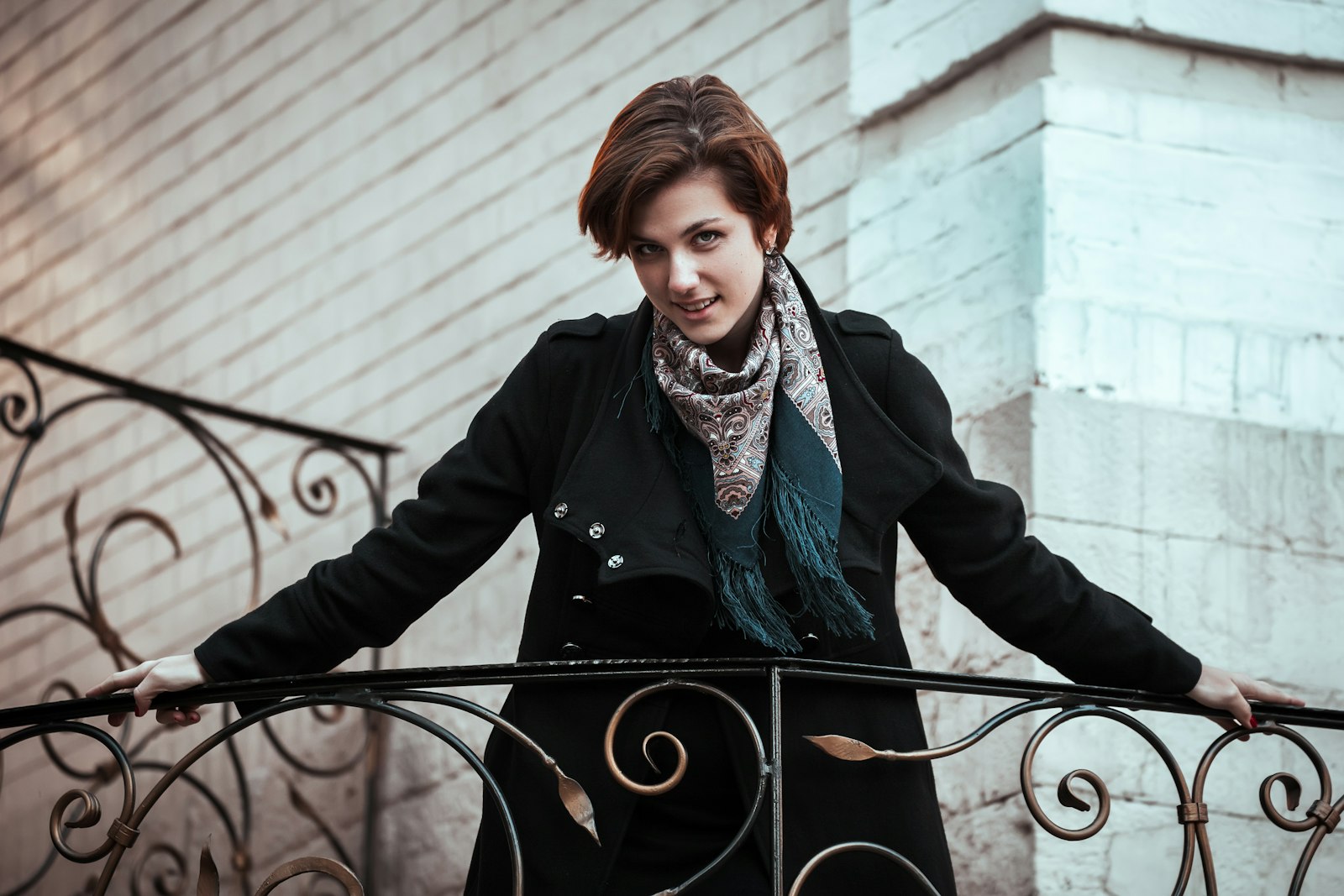 Woman in a long black coat standing beside a black metal fence, women's fall coat trends 2026