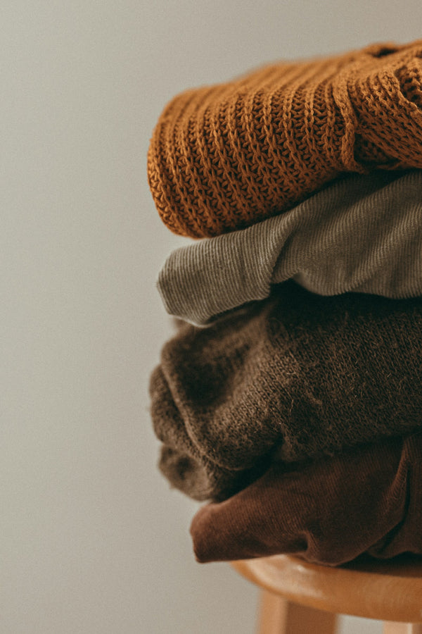 Folded knit sweaters stacked on a wooden stool
